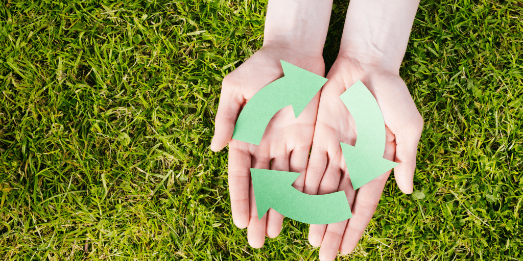 Moebius loop din carton verde in mainile unei femei care tine mainile deasupra unui loc cu iarba verde
